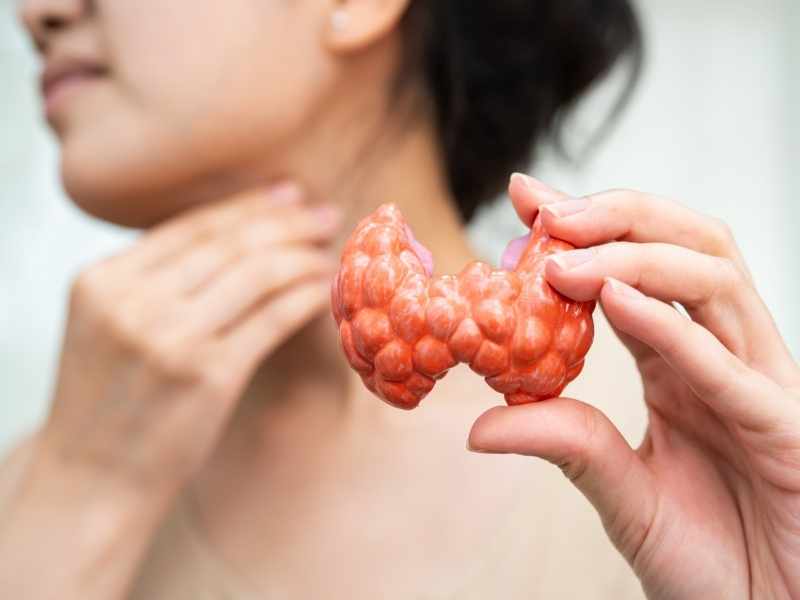 mujer tocándose el cuello sosteniendo con una mano una figura que representa a la glándula tiroidea