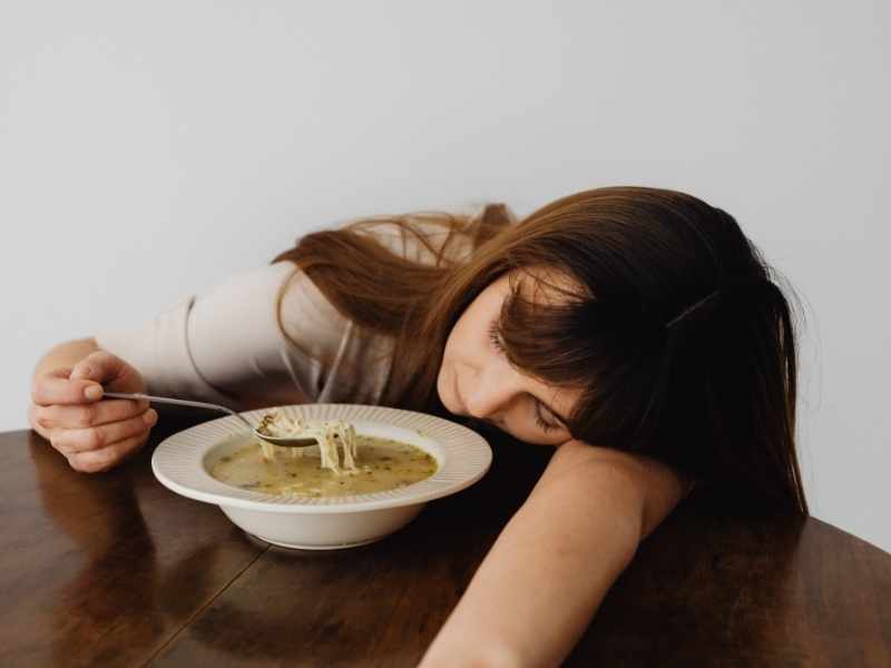 mujer durmiendo a un lado de su plato de sopa, por pesadez después de comer